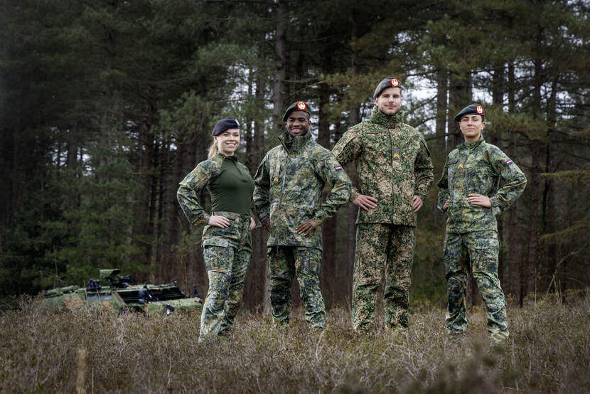 4 Militairen poseren met het nieuwe tenue voor de landmacht met bomen op de achtergrond.