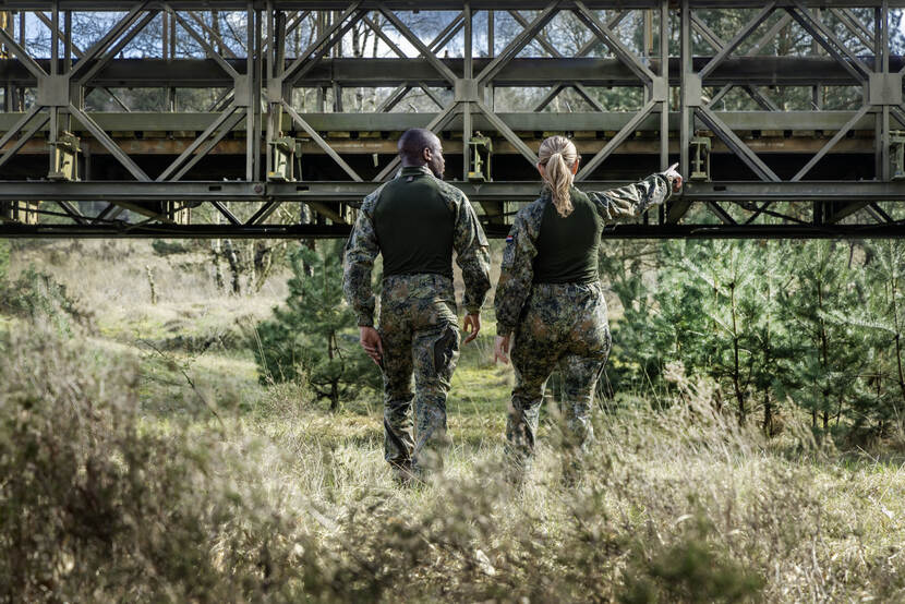 Een mannelijke en een vrouwelijke militair in het nieuwe tenue op de rug gezien voor een brug.