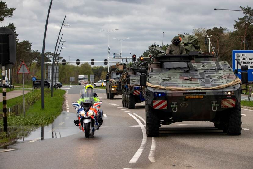 Militaire voertuigen rijden over de weg geflankeerd door een motor van de marechaussee.