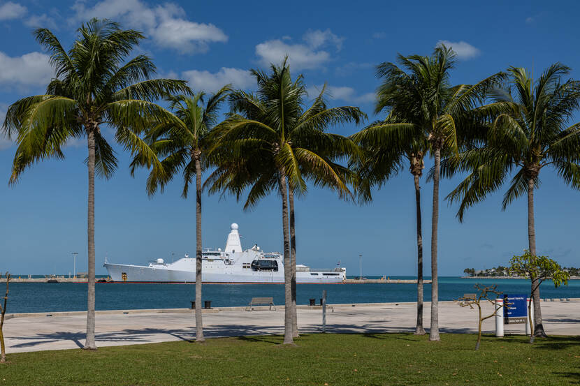 Stationsschip Zr.Ms. Groningen in de haven van Key West met palmbomen op de voorgrond.