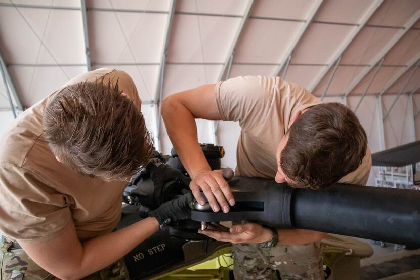 2 militairen bezig met montage van deel van een Chinook.