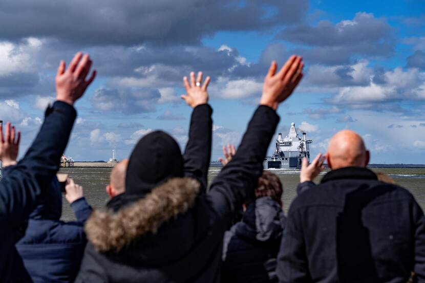 Mensen zwaaien een vertrekkend marineschip uit.