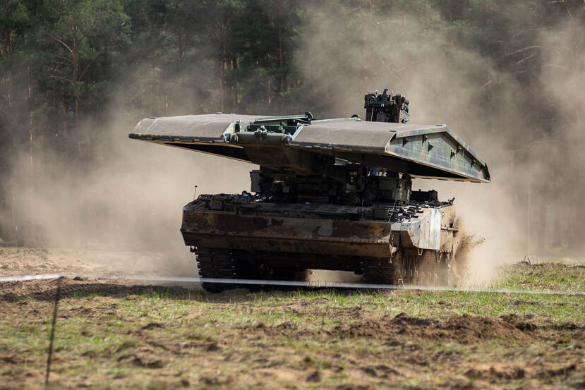 Leopard-tank vervoert brugdeel. Rondom opstuivend zand.