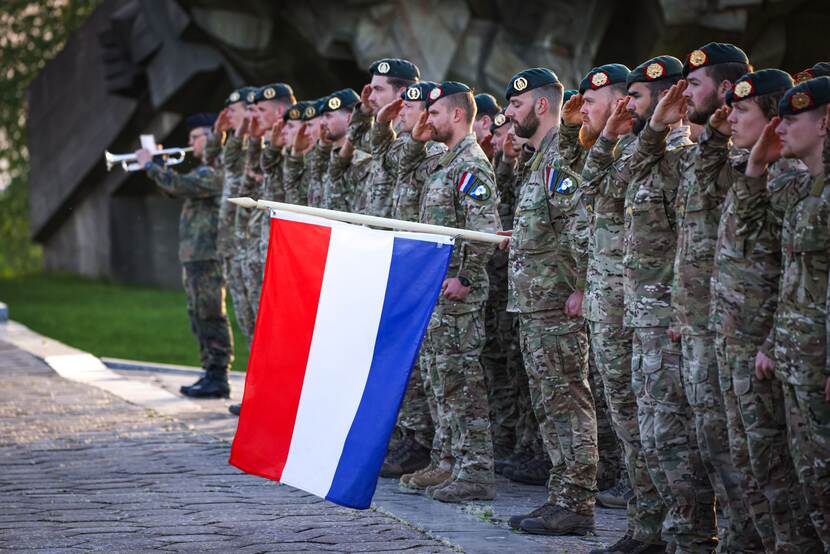 Rij Nederlandse militairen brengt eregroet met Nederlandse vlag tussenin.
