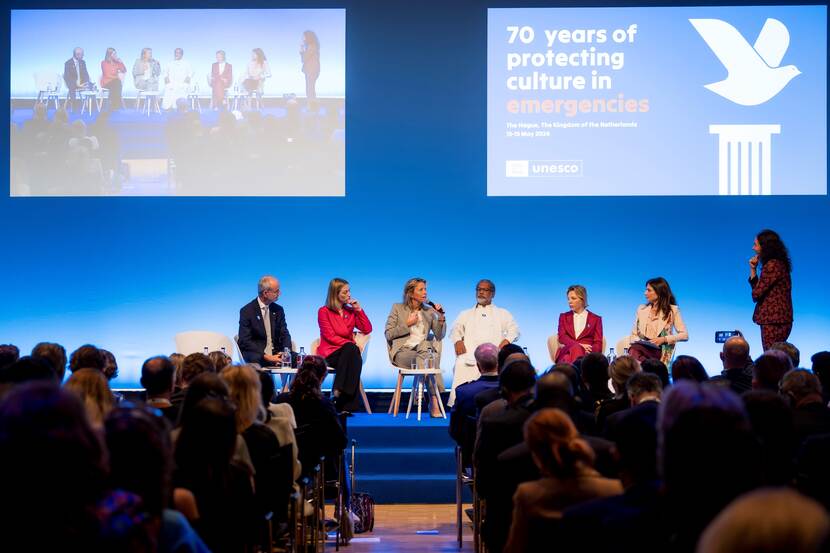 Minister zit met nog 5 mensen op een podium tijdens paneldiscussie bij bijeenkomst 70 jaar bescherming cultureel erfgoed tijdens conflicten.