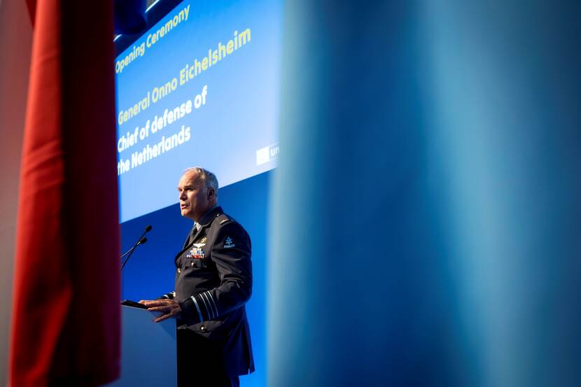 Commandant der Strijdkrachten generaal Onno Eichelsheim spreekt op podium bij openingsceremonie. Hij is te zien tussen 2 vlaggen.