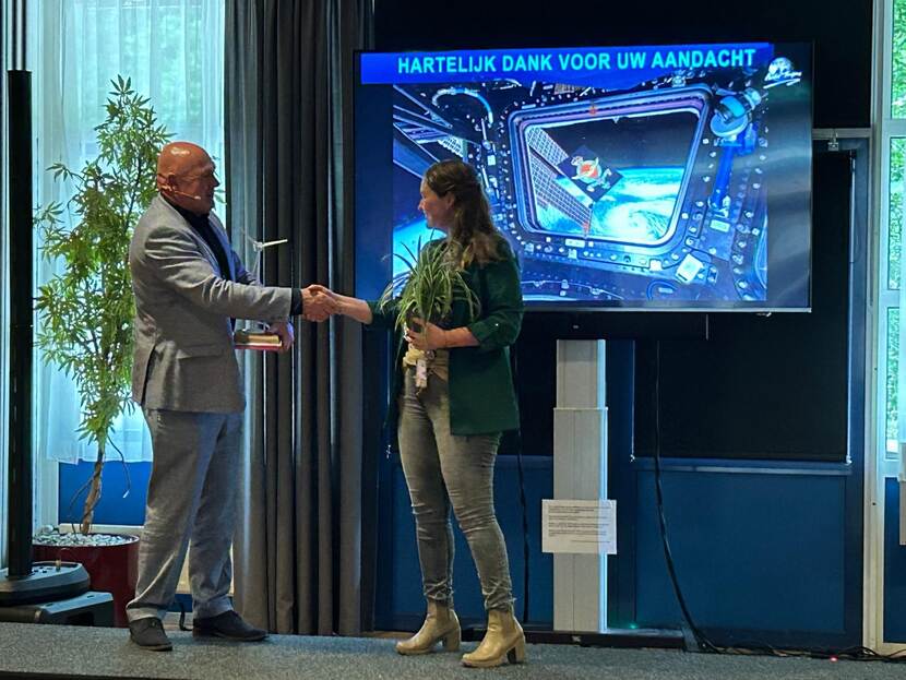 Astronaut André Kuipers schudt op een podium de hand van een vrouw. Aan het eind van een presentatie waarin het publiek wordt bedankt voor hun aandacht.