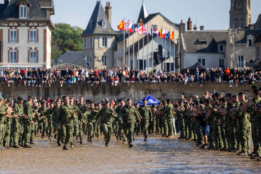 De nieuwe fuseliers rennen door een haag van collega’s de zee in. Op de achtergrond kijken toeschouwers mee naar de traditie.