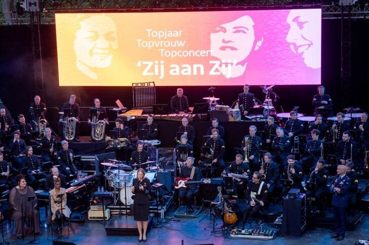 Orkest bij concert. Tekst op scherm: Topjaar, topvrouw, topconcert Zij aan Zij.