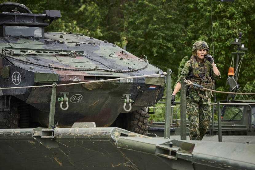 De koningin loopt voor een militair voertuig.