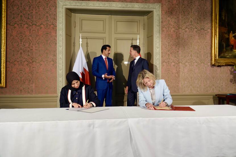 Kajsa Ollongren en Lolwah Al Khater zitten aan een tafel en tekenen de overeenkomst. Achter hen staan de Emir van Qatar en Mark Rutte.