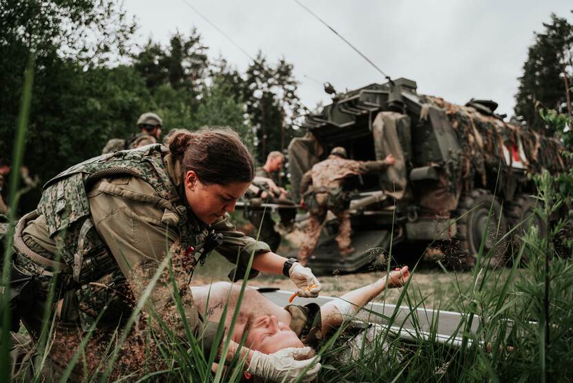 Militair buigt zich over een gewonde collega. Op de achtergrond gepantserde ziekenauto.