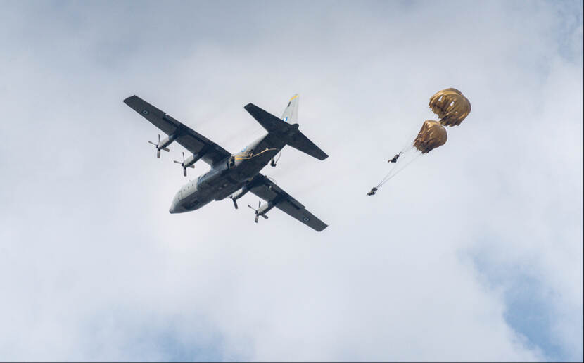 Parachutist springt uit een C-130 transportvliegtuig tegen een bewolkte lucht.