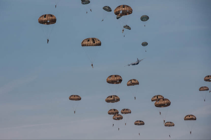 Een groep parachutisten springt uit een vliegtuig.