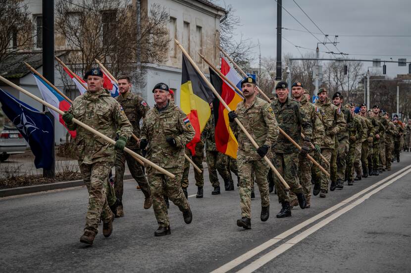 Rij militairen marcheert op straat met vlaggen.
