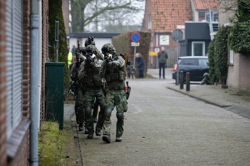 Militairen lopen met getrokken wapens door een straat.