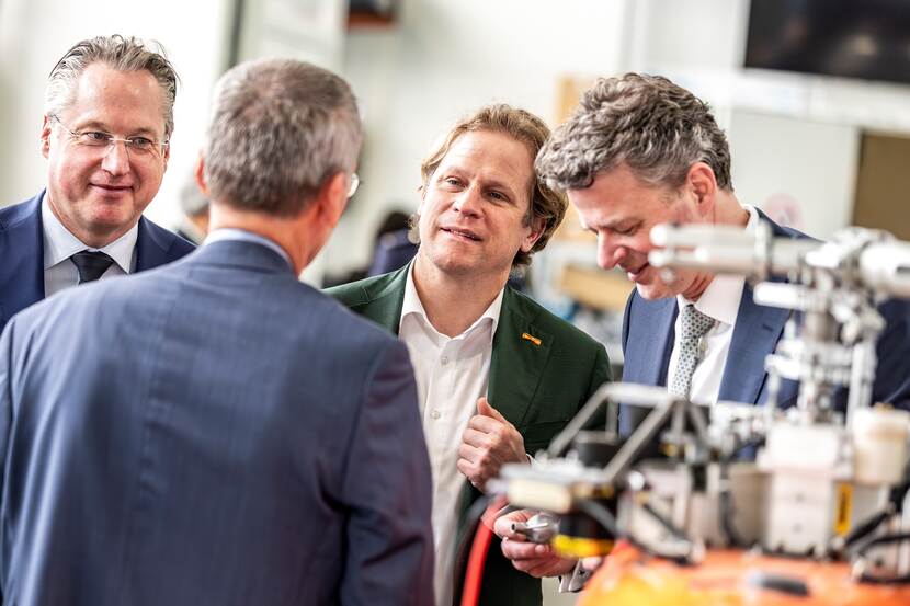Gijs Tuinman in gesprek met 3 mannen. Op voorgrond niet te identificeren apparaat.