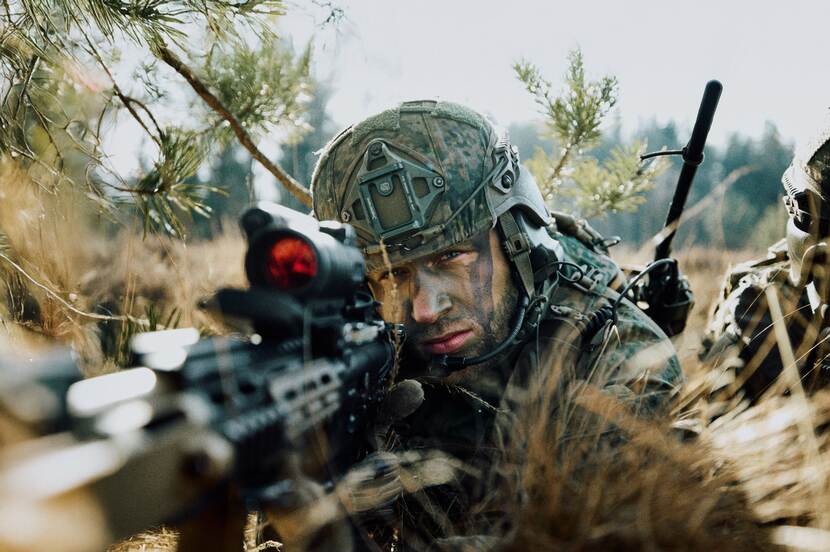 Een militair in de bosjes gebruikt een wapen.