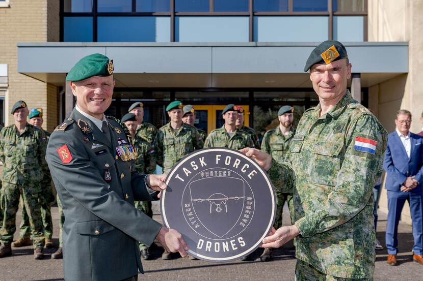 2 militairen houden een bord vast, met daarop een logo van de taakgroep drones.