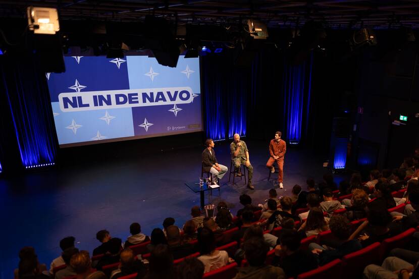 3 mannen van het bureau De Kiesmannen zitten op het podium voor een publiek.