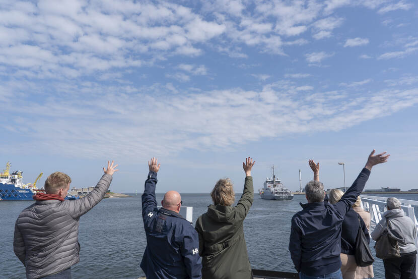 Mensen zwaaien een vertrekkend marineschip uit.
