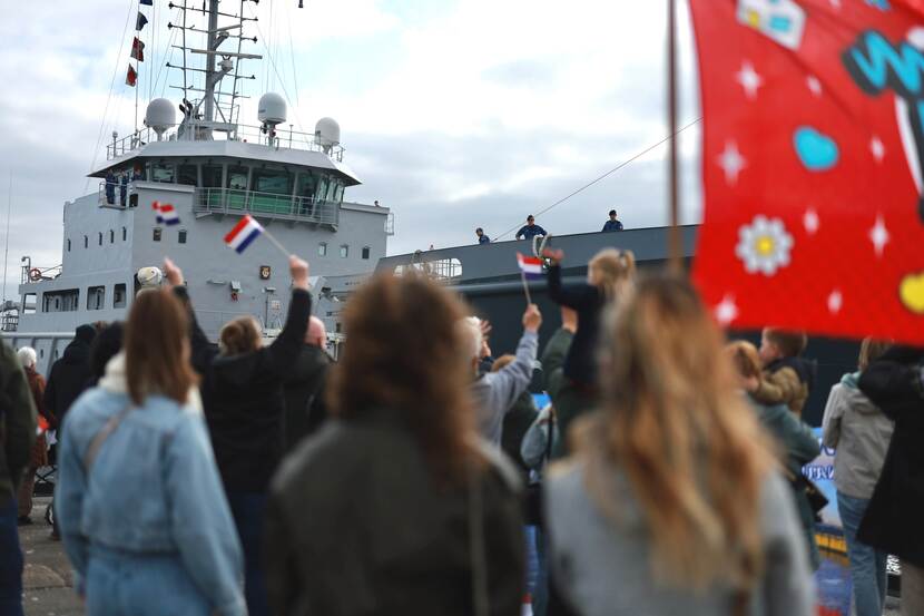 Mensen zwaaien op kade naar binnenvarend marineschip.