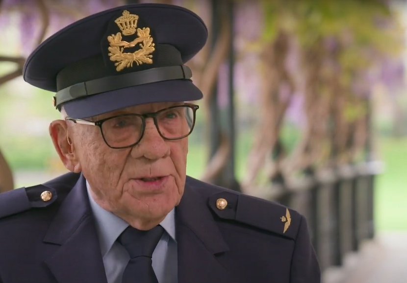Een oude man in een blauw luchtmachtpak praat tegen een interviewer, die buiten beeld zit.