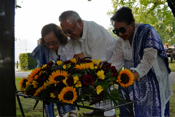 Drie mensen leggen een krans met zonnebloemen voor het monument.