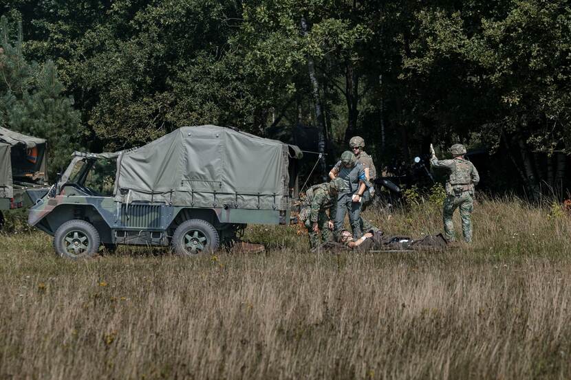 Militairen met gewonde op draagbaar bij militaire ambulance.