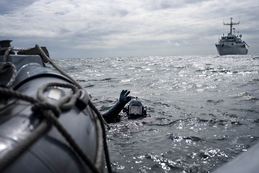 Een duiker in zee naast een marineschip.