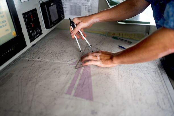 Een marinier is aan het werk met een kaart, een passer en een geodriehoek.