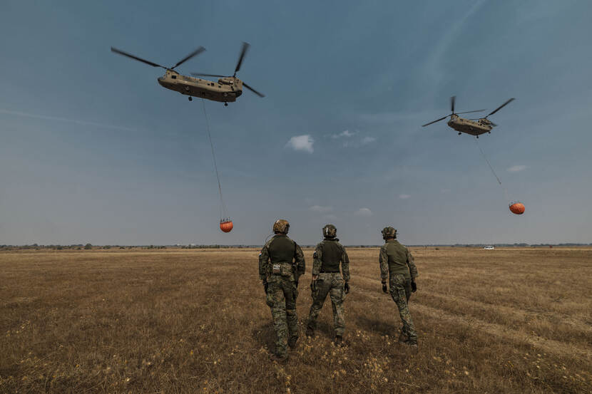 Militairen kijken naar de helikopter die wegvliegt met een bambi bucket