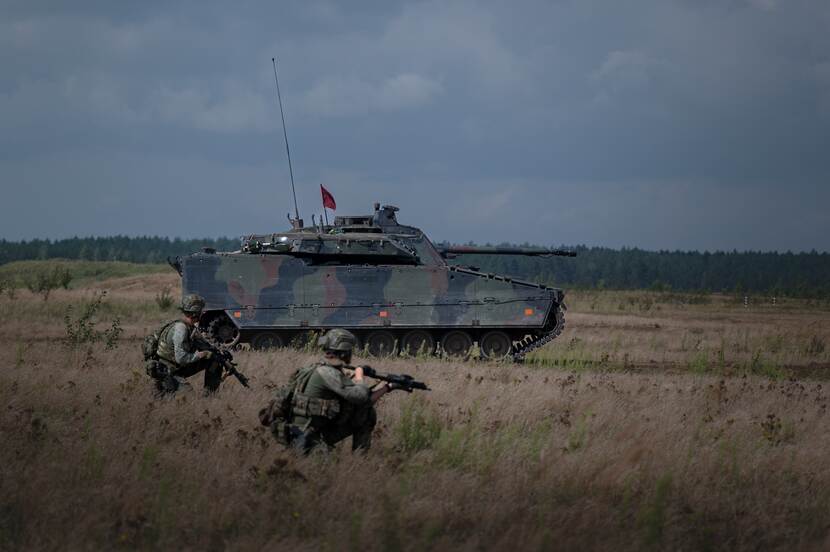 Militairen met wapens gehurkt voor een CV90.