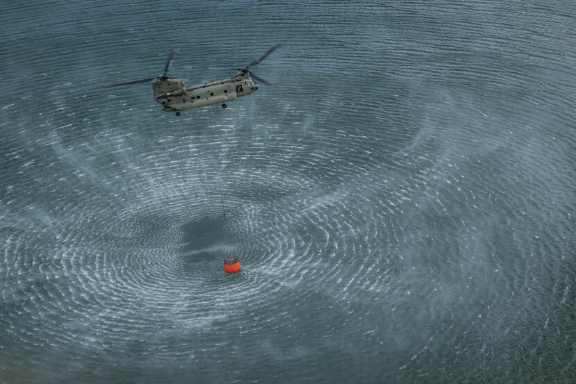 Cirkels op het water van een Chinook-helikopter die net een oranje bambi bucket met water heeft gevuld.