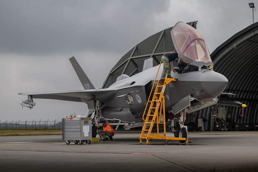 Een gele trap staat bij de geopende cockpit van een F-35. Een militair staat bovenaan de trap en is op het punt om in het toestel te stappen.