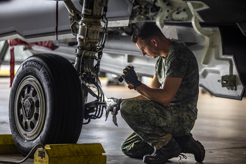 Technicus zit geknield naast een wiel van een F-35. Hij schijnt met een zaklamp.