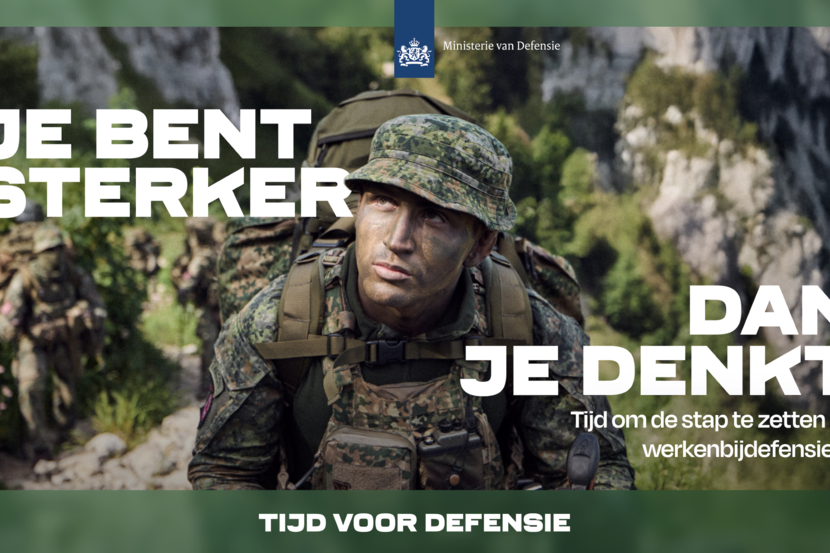 Militair met groen geschminkt hoofd en hoedje op en rugzak op zijn rug met rotsachtig landschap en bomen vaag te zien op de achtergrond.