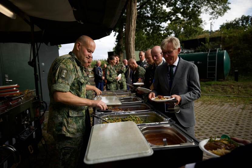 Een militair schept eten op uit warmhoudbakken voor de deelnemers.