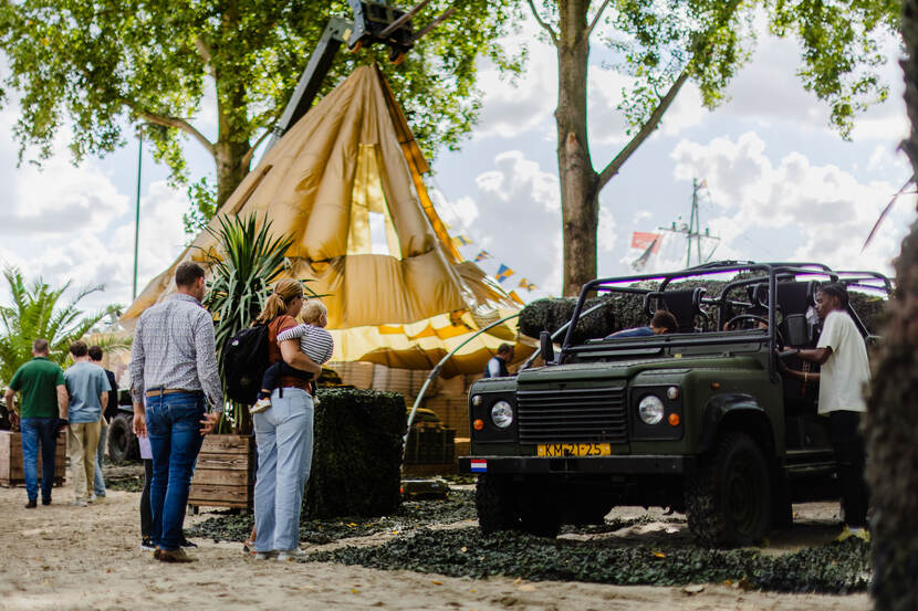 Een man, vrouw en klein kind op de arm van de vrouw staan bij een jeep van de marechaussee.