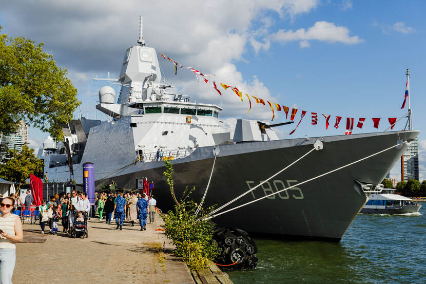 Het grijze schip de Zr.Ms. Evertsen, versierde met vlaggetjes, ligt aan de kade. Op de kade lopen veel bezoekers van de Wereldhavendagen.
