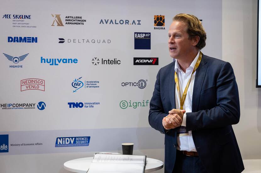 De staatssecretaris houdt een toespraak. Achter hem zijn de namen van een aantal bedrijven zichtbaar.