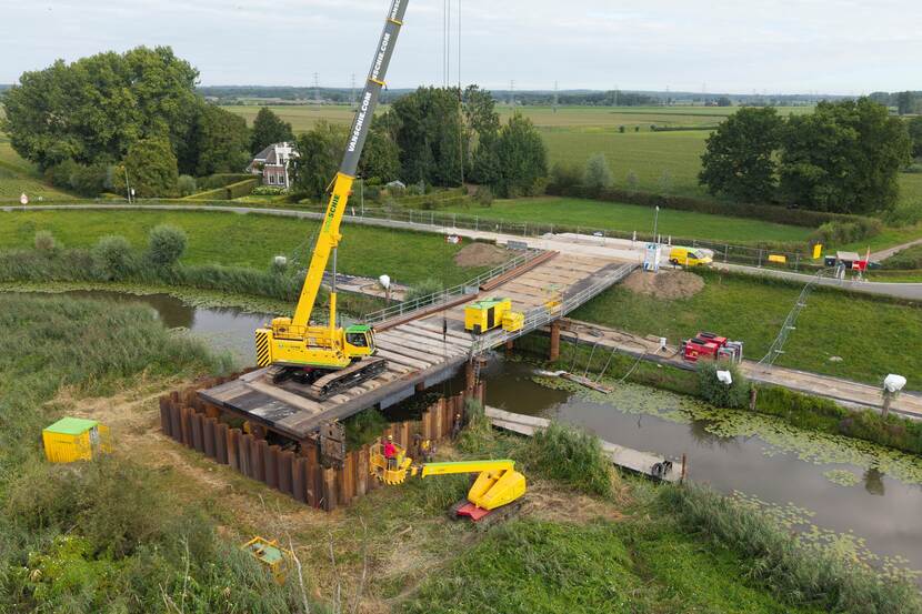 Hijskraan en tijdelijke brug van platen over de rivier.