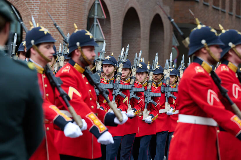 Marcherende militairen in rode jasjes.