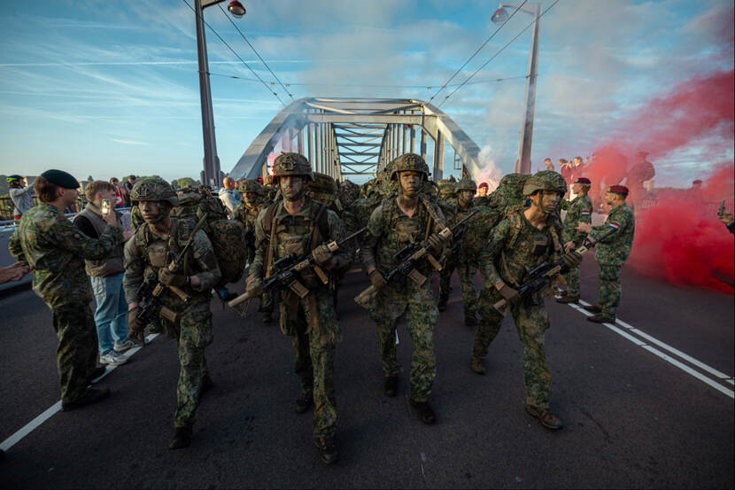 Militairen in volle bepakking marcheren over brug.