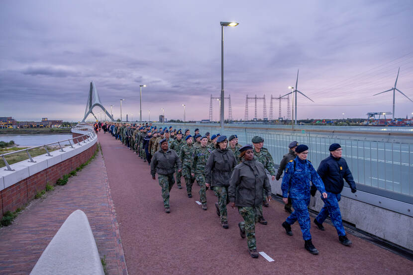 Militairen lopen over een brug, vrouwen voorop.