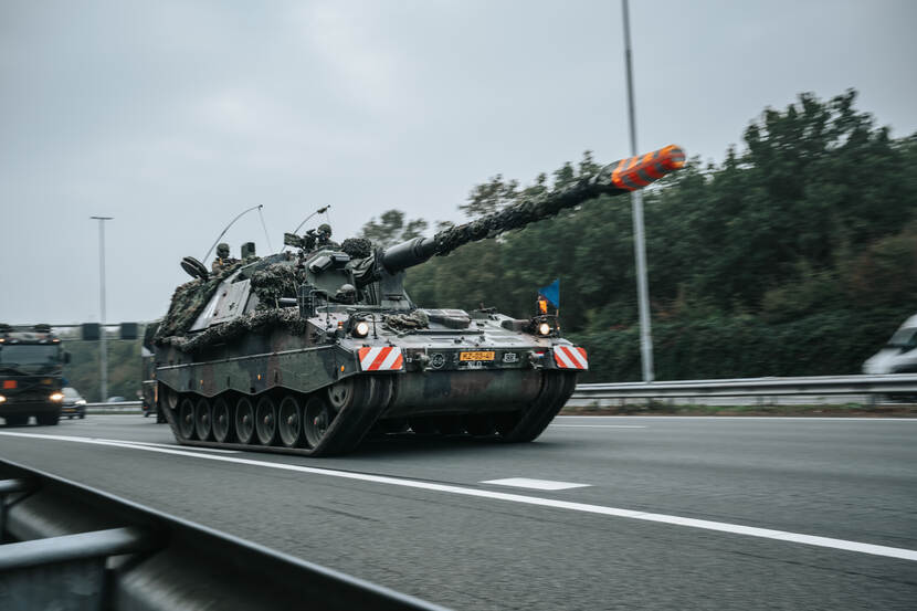 Een Pantserhouwitser rijdt over snelweg. Daarachter is een vrachtwagen te zien.