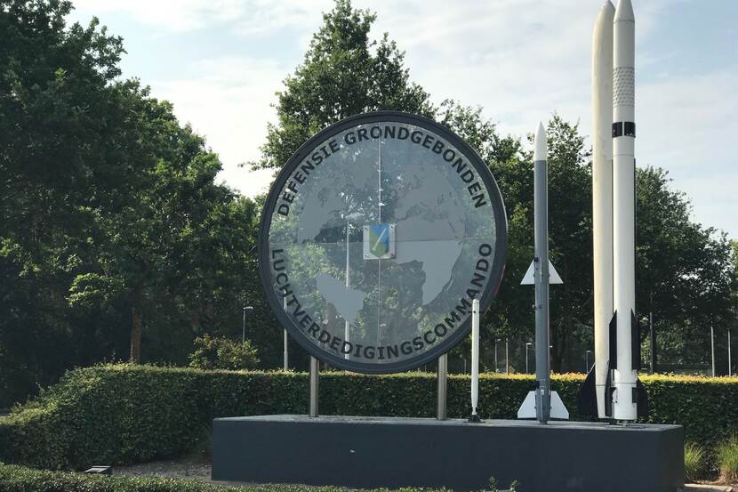 Ingang kazerne met groot rond bord met logo en tekst Defensie Grondgebonden Luchtverdedigingscommando.