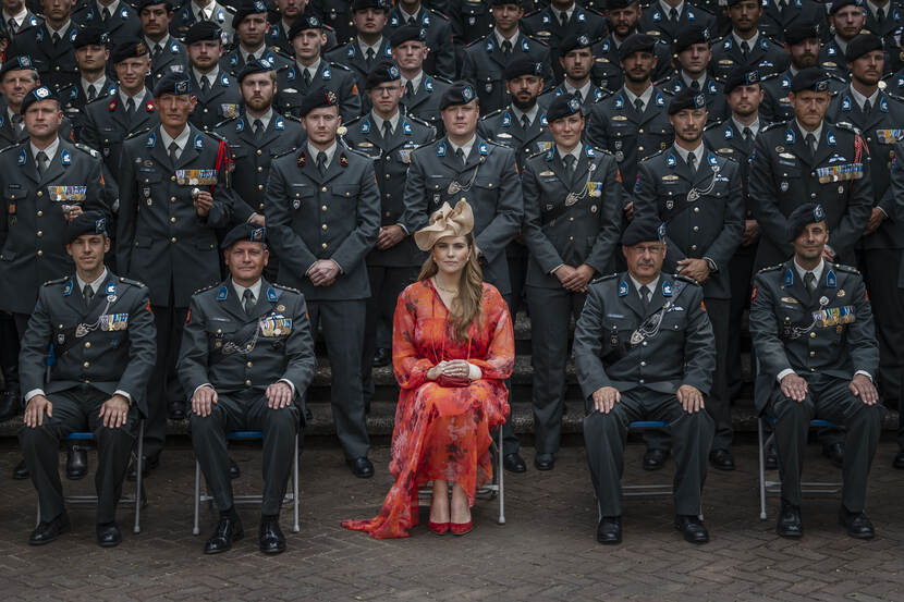 Prinses Amalia in een oranje gewaad zit op een kruk. Om haar heen tientallen landmachtmilitairen in uniform.