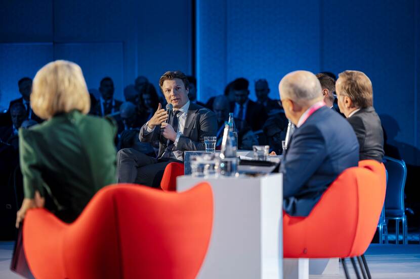 Minister Brekelmans tijdens paneldiscussie met ambtgenoten. Deelnemers zitten op oranje stoelen.