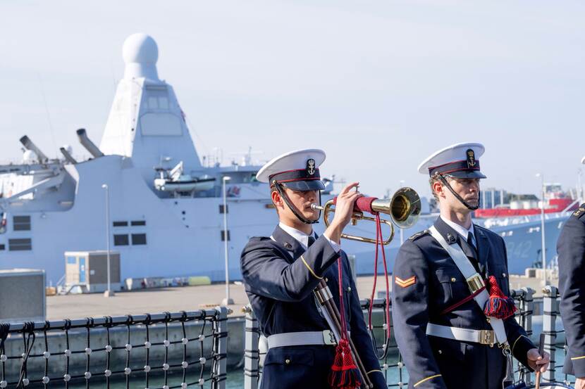 2 mariniers, een blaast op een trompet. Op de achtergrond het schip Zr.Ms. Den Helder.